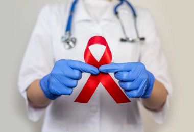 AIDS ve HIV dünya desteği için kırmızı kurdele, yakın çekim. Kadın doktorun eli..