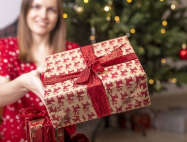 Kırpılmış beyaz kadın elinde Noel hediyeleri ya da kırmızı kurdele ve fiyonkla kağıda sarılmış hediyeler taşıyor. Bir kutuyu kapat.