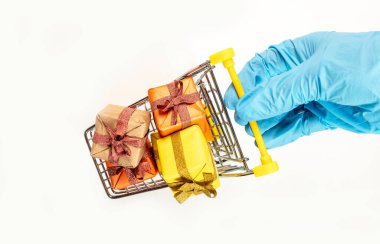 Cart or trolley full of wrapped gift boxes. Basket with presents for christmas held by hand in protective glove isolated on white background, top view. Safe shopping for new year.
