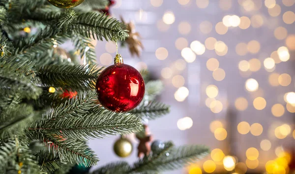 Close up view of beautiful fir branches with shiny red bauble or ball, xmas ornaments and lights, christmas holidays background.