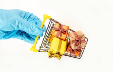 Cart or trolley full of wrapped gift boxes. Presents for christmas held by hand in protective glove isolated on white background, top view. Safe shopping for new year, top view