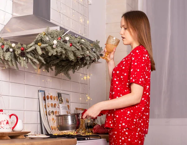 Woman drinking champagne alone at home while cooking christmas dinner at decorated kitchen for xmas and new year. Female in home clothes.