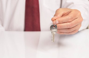 Kravatlı bir işadamının eli, beyaz masanın üzerinde duran ve yansıması olan yeni bir daireden anahtar veriyor..