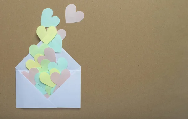 Papieren harten van verschillende kleur verspreid van witte envelop over bruine ambachtelijke achtergrond met kopieerruimte — Stockfoto