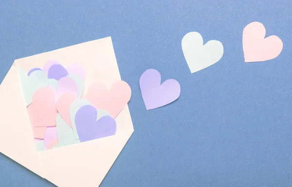 Papieren harten van verschillende kleur verspreid van witte envelop over blauwe achtergrond — Stockfoto