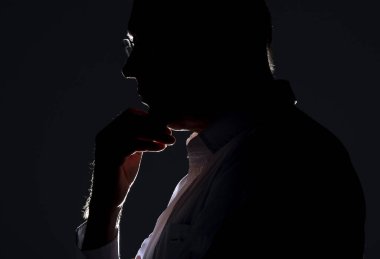 Arka ışıklandırmalı ve gözlüklü bir erkek silueti. Gözlüklü düşünceli adam.