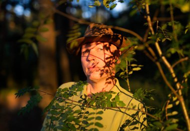 Ağaç dallarının gölgeleri ve yapraklarıyla aydınlanan olgun bir adam..