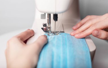 Makineye yüz maskesi dikerken ellerinizi kapatın. Kadın elleri.