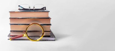 Büyüteci ve beyaz arka planda gözlüğü olan bir yığın kitap. Metin için alanı olan pankart