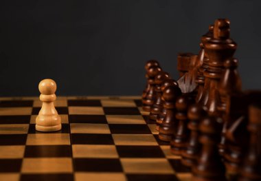 Bir beyaz piyon satranç tahtasındaki siyah satranç figürlerine karşı. Cesur karar kavramı.