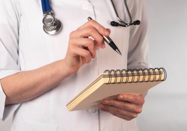 Tıp üniformalı kadın elinde kalemle defterini işaret ediyor..