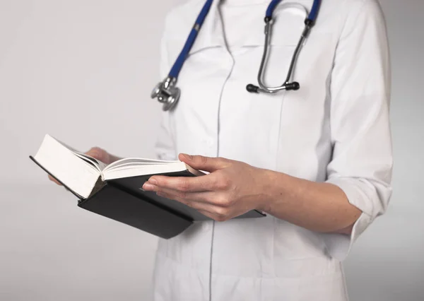 Female doctor or medical student in uniform reading thick book on medicine, prepare for exam.