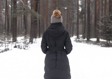 Karlı ormanlarda yürümekte olan ponponlu şapkalı bir kadın. Kar havasında tek başına..