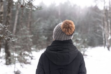 Karlı ormanlarda yürümekte olan ponponlu şapkalı bir kadın. Kar havasında tek başına..