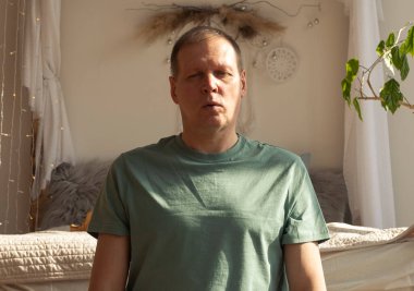 Evde yoga ve nefes kontrolü yapan bir adam, rahat bir yatak odasında meditasyon yapıyor..