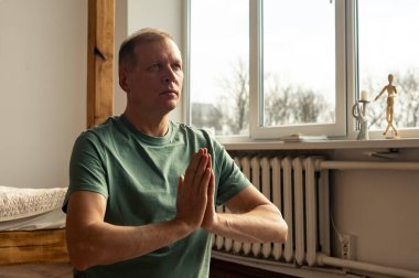 Olgun bir adam yoga yapıyor ve sıcacık bir evde meditasyon yapıyor. El ele tutuşuyor.