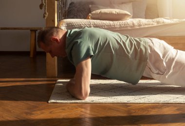 Olgun beyaz adam evde egzersiz yapıyor, kalas egzersizi yapıyor, paspas üzerinde antrenman yapıyor..