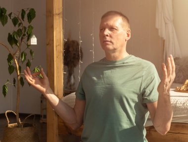 Olgun bir adam, meditasyon poziyonuyla rahat bir evde yoga ve meditasyon yapıyor.