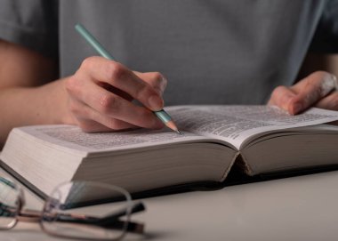 Bayan öğrenci elleri kitaptaki bilgilerin altını çizer, sınava hazırlanır, kalem tutarlar. Eğitim kavramı