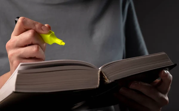 Female student hands holding yellow highlighter and reading book or textbook, making notes, underlines, prepare for exam at table at night. Education concept