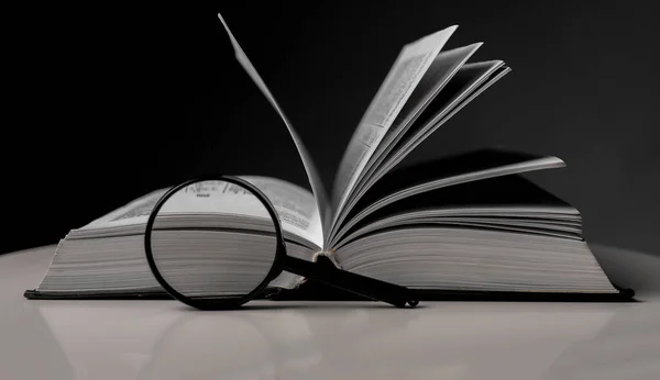 Kitabı sayfaları çevirip büyüteçle kapat. Hardcover 'lı ders kitabı masanın üstünde. Eğitim ve araştırma kavramı