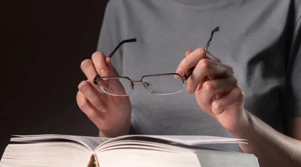 Mãos de estudante do sexo feminino fechar, segurando óculos e livro ou livro didático, à procura de informações e leitura à noite — Fotografia de Stock