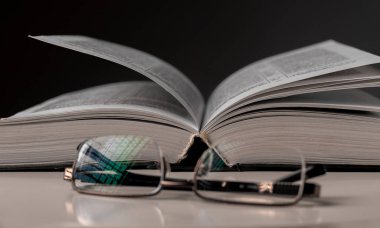 Gözlük ve siyah arkaplan üzerine açık bir kitap. Eğitim kavramı