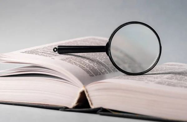 Open book closeup with turning pages and magnifying loupe. Textbook in hard cover on table. Studying and research concept