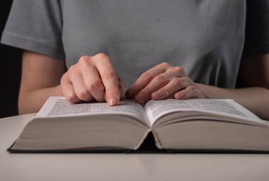 Kadın öğrenci elleri kapalı, kitaptaki ya da kitaptaki metne işaret ediyor, bilgi arıyor ve geceleri okuyor.