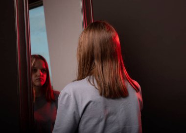 Genç bir kadın kederle aynadaki yansımasına bakıyor. Mutsuz üzgün kişi. Psikolojik zihinsel bozukluklar ve kendine saygı kavramı