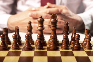 Satranç taşları ve arka planda erkek eli olan satranç tahtası. İş stratejisi kavramı