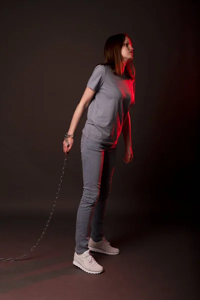 Kobieta związana łańcuchem chodzącym po czarno-czerwonym tle. Pojęcie długów, ograniczeń, strachu — Zdjęcie stockowe