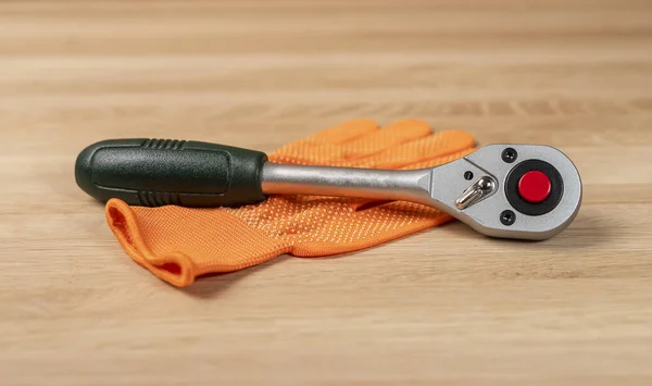 Building glove with socket ratchet handle. Industrial metal tool, close up on wooden background — Stock Photo, Image