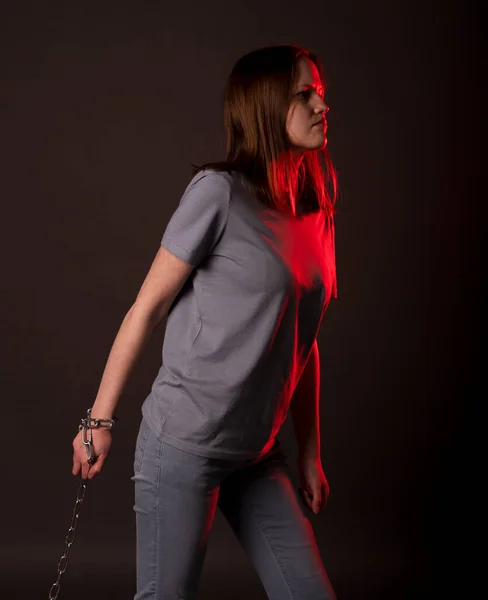 Woman tied with chain walking over black and red background. Concept of debts, bounds, fear.