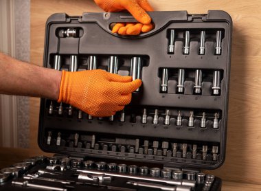 Alet kutusundan alınmış soket mandal saplı eldiven giymiş bir erkek. Endüstriyel metal alet, ahşap zemine yakın..