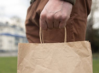 Elleriniz organik kahverengi el sanatları paketini tutarken ya da şehir ve çimen arka planında el ele tutuşurken. Çevre yaşamı.