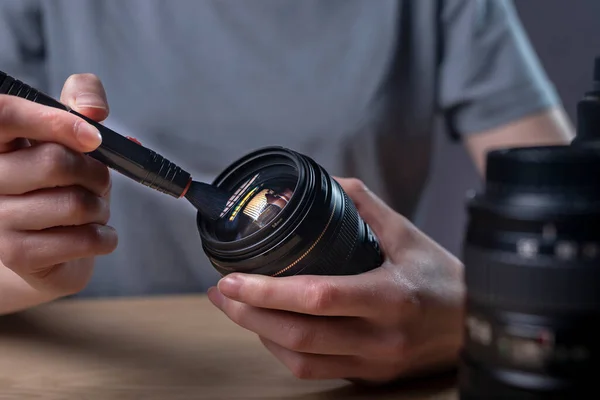 Person cleaning camera lens with black professional brush, close up, removing dust.