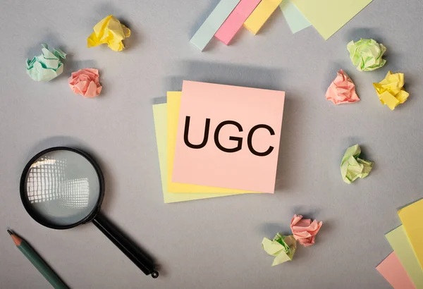 UGS or User-generated content acronym for social media on colorful bright pastel sticky notes, desk with stationary, top view.