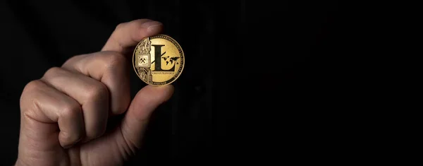Litecoin golden coin in male hand over black background. Banner with space for text — Stockfoto