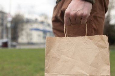 Erkek el, şehir ve çimen arka planında organik kahverengi el işi paketini tutuyor. Eko yaşam biçimi