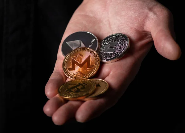 Monero en andere onverschillige cryptogeld munten in mannelijke hand over zwarte achtergrond, close-up — Stockfoto