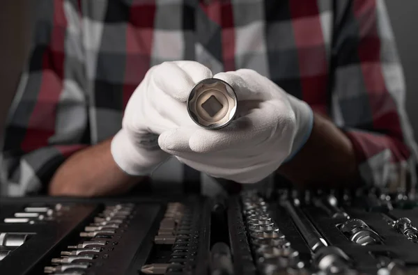 Male hand in white building gloves with metal steel hex socket, hexagon metal head. Car repair metal tool, close up