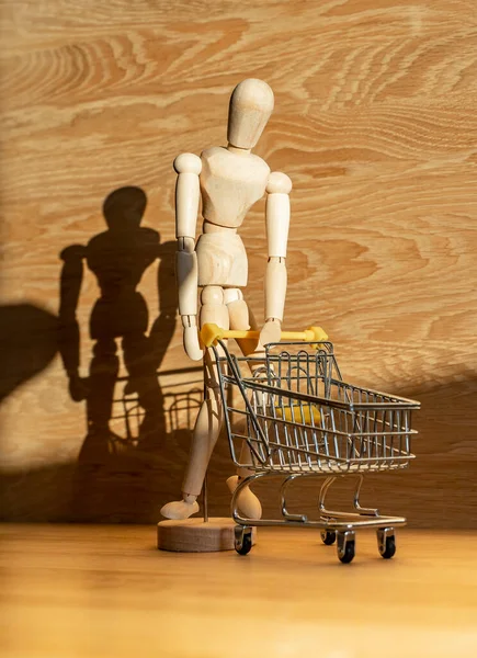 Fardeau du concept de shopping, crise. Homme en bois penché et penché sur le chariot de magasin dans la belle lumière du jour — Photo