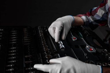 Erkek eller beyaz inşaat eldivenleriyle araç ve ev onarımı için çeşitli metal aletlerle açık alet çantasının üzerinde, yakın plan.