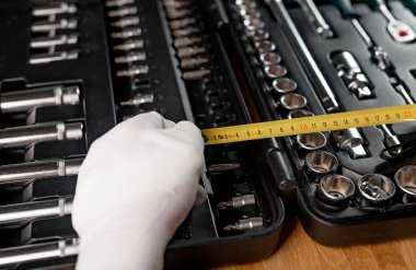 Sarı geri çekilebilir mezura açık alet çantasının üzerine eldivenle erkek ellerine yayılmış.