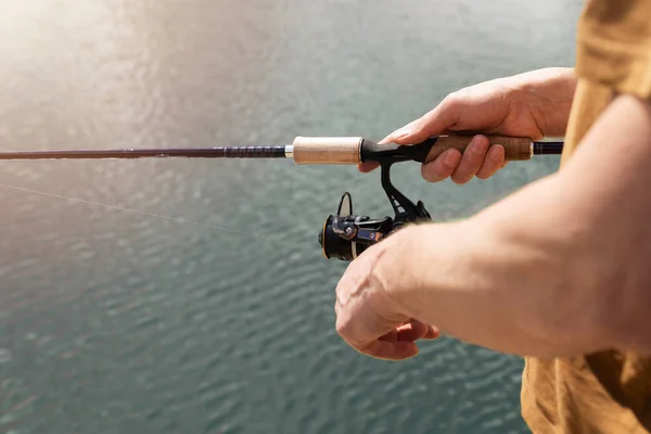 Mains mâles hoolding spinning rod, cuillère-appât et la pêche sur l'eau bleue, gros plan — Photo
