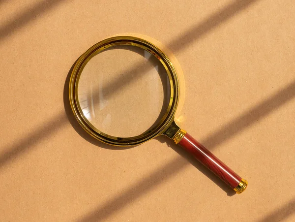 Gold magnifying glass over craft brown background with day light. Search tool concept — Stock Photo, Image