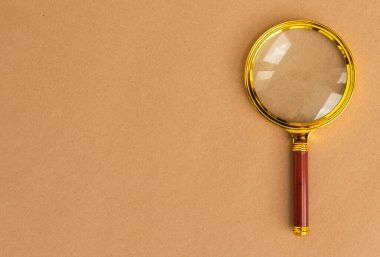 Kahverengi karton arka planda altın büyüteç. Metin için kopyalama alanı olan arama aracı