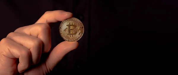 Glänsande bitcoin BTC gyllene mynt i manlig hand över svart bakgrund. Lite kryptovaluta. Banner med kopieringsutrymme för text — Stockfoto