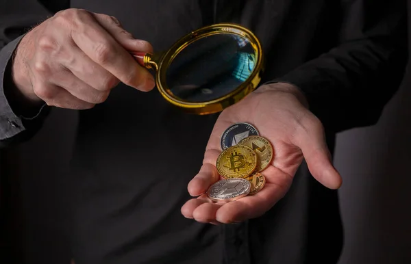 Golden and silver coins of crypto currency in male hand palm with magnifying glass, close up. Pile of bitcoin and other cryptocurrency — Stockfoto